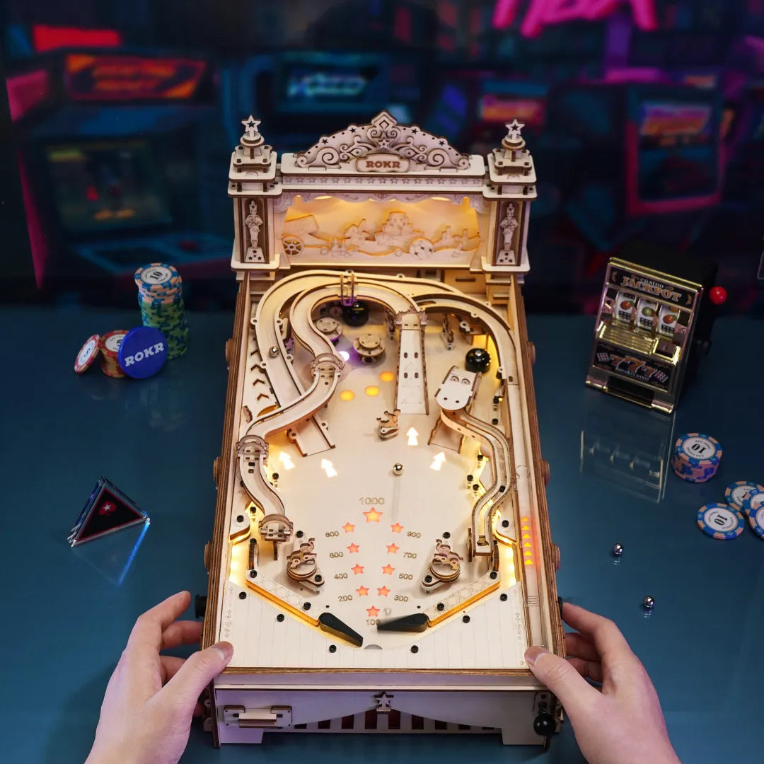 ROKR 3D Pinball Machine wooden puzzle top-down view with warm LED lighting showing the full playfield with bumpers, ramps, scoring stars, and an ornate decorative cabinet header