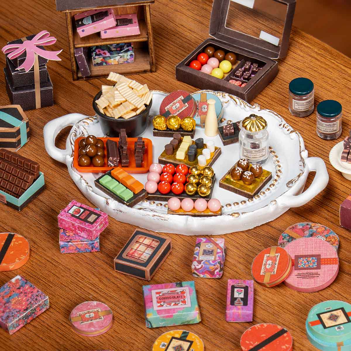 Rolife Henry's Chocolate miniature house DG174 top-down view showing an elaborate miniature chocolate shop tray filled with tiny chocolate shapes, gift boxes, colorful tins, and candy replicas.