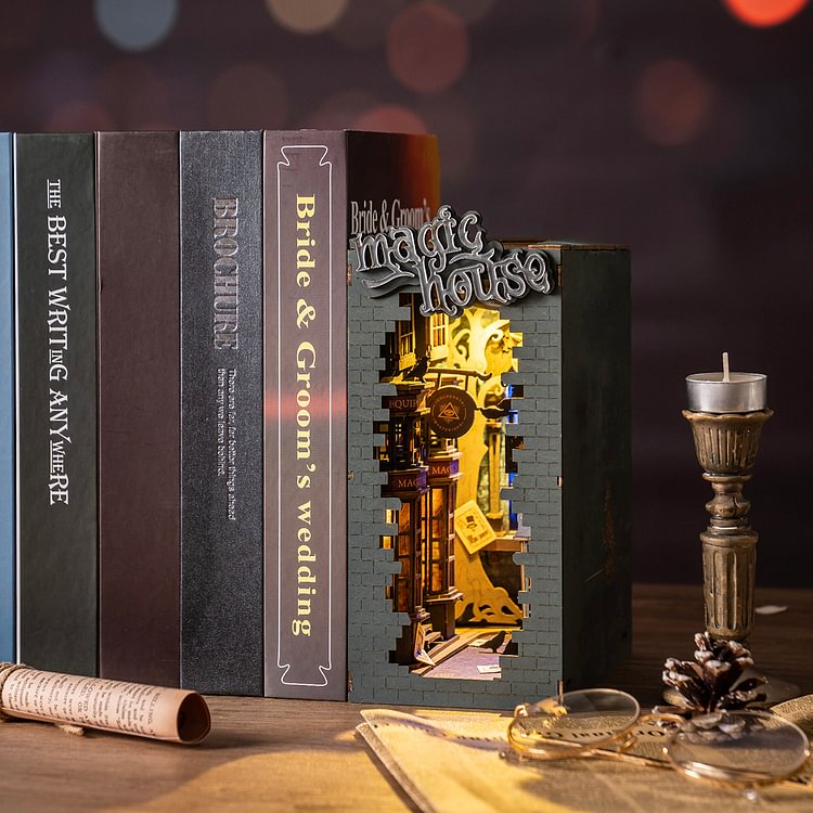 Rolife Magic House book nook glowing between dark books, with a brass candlestick and compass on a wooden desk