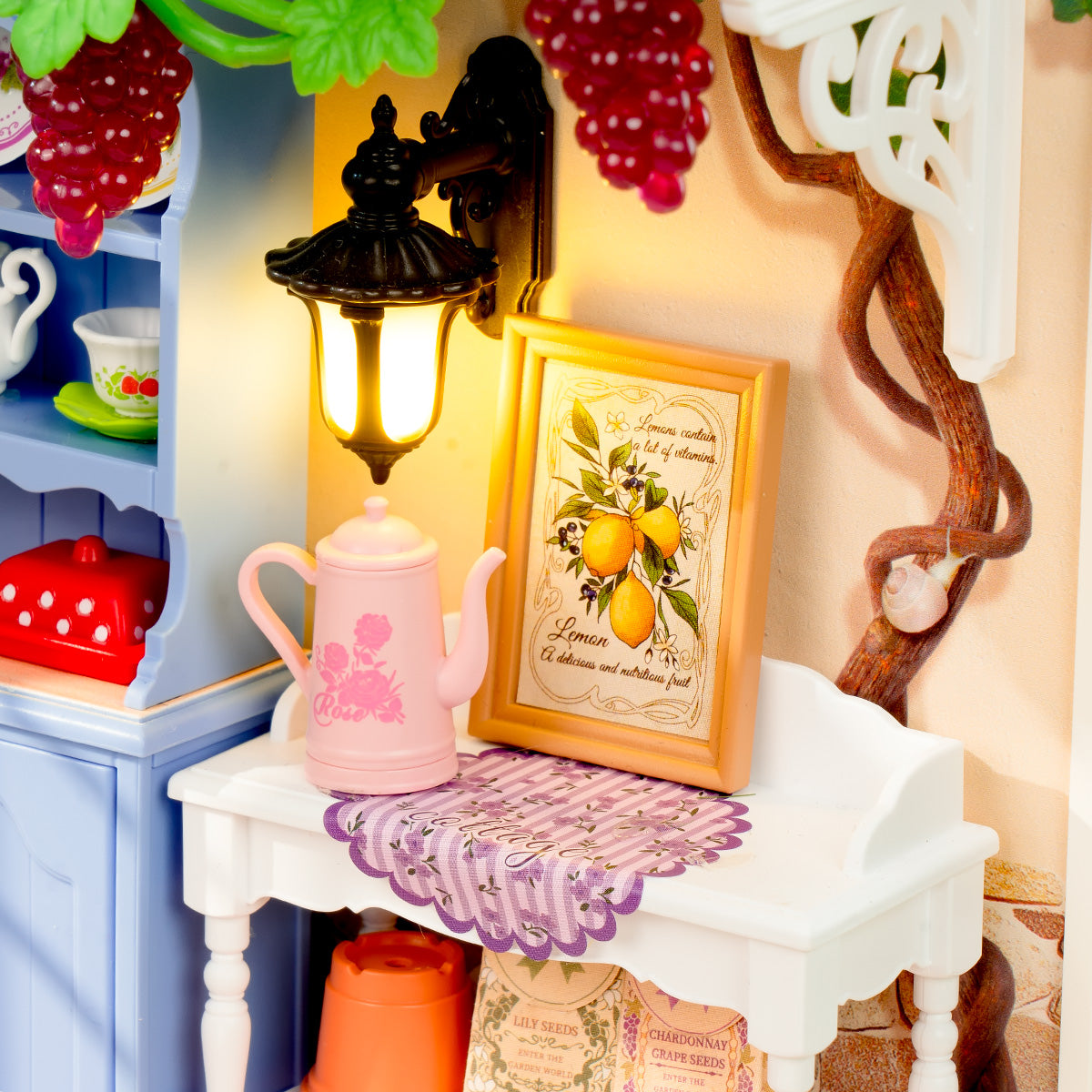 Rolife Midsummer Dream Yard DW025 detail of warm-lit side table with pink watering can and lemon art print beside a glowing wall lantern