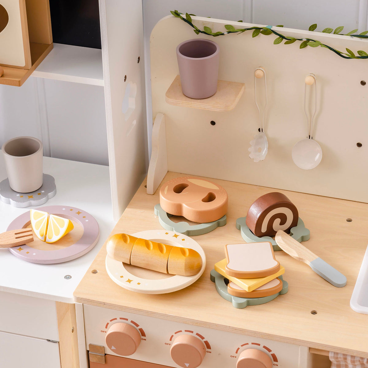 ROBUD wooden bread playset on natural wood play kitchen countertop with baguette on plate, pretzel, swiss roll and toast stack with cheese slice, and wooden fork visible