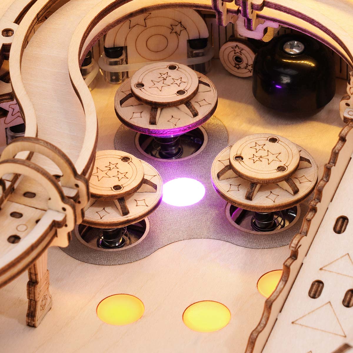 Close-up of the ROKR 3D Pinball Machine wooden puzzle bumper zone showing three mushroom-shaped wooden bumpers with star engravings lit by a purple LED glow