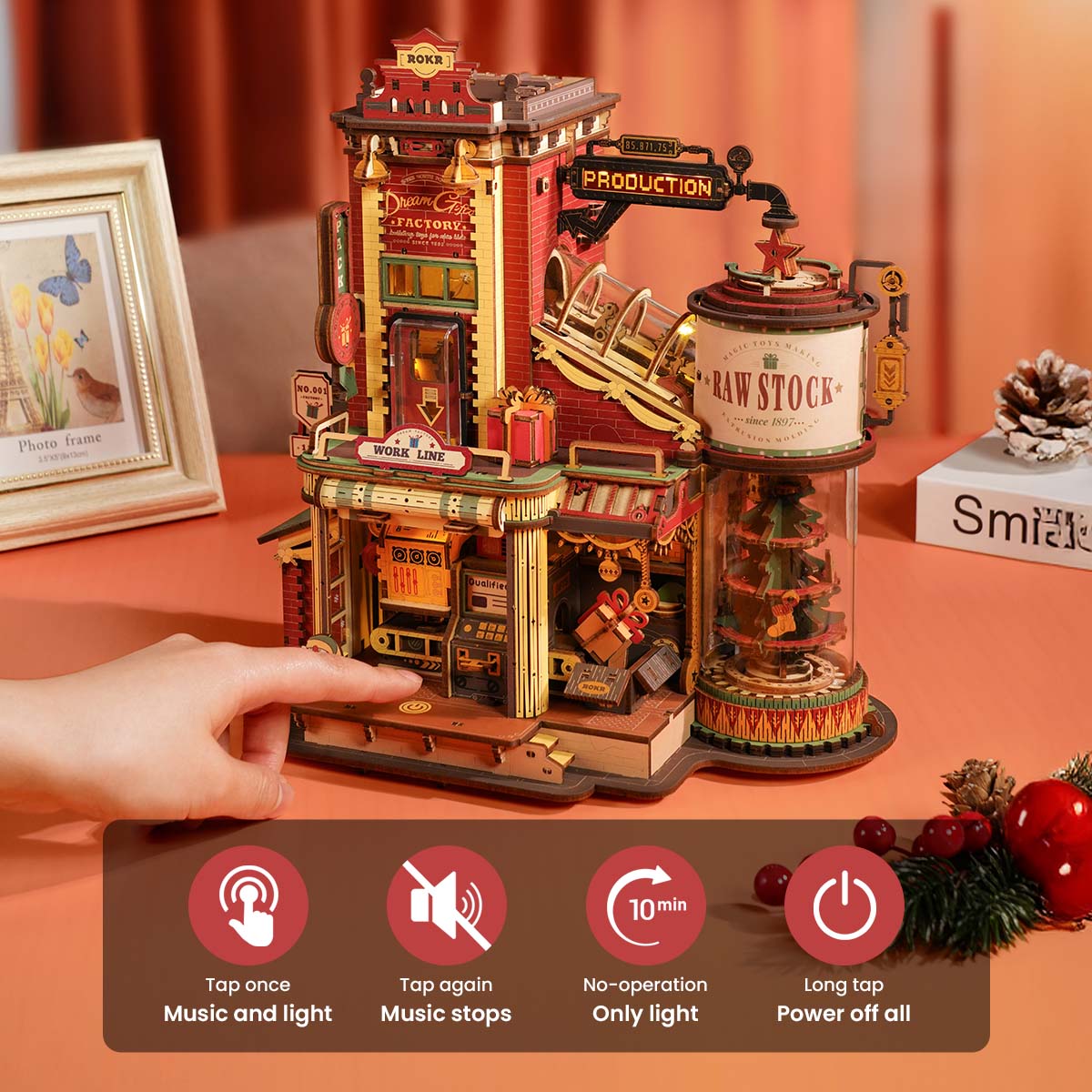 ROKR Dream Gift Factory wooden music box EAB01 full angled view showing the lit up production floor and Raw Stock tower beside decorative Christmas foliage.