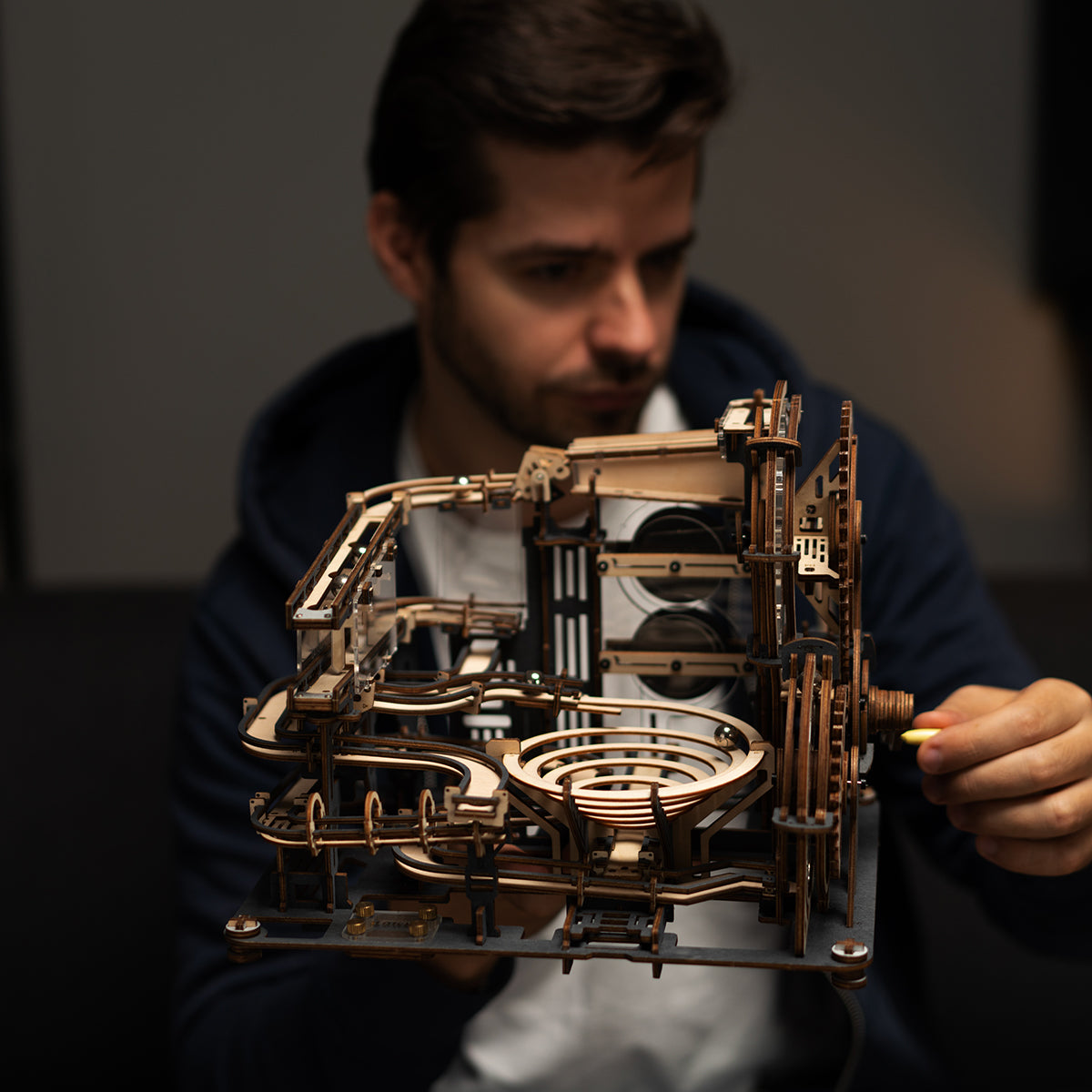 Man in blue sweater holding the assembled ROKR Marble Night City marble run with both hands against a dark background