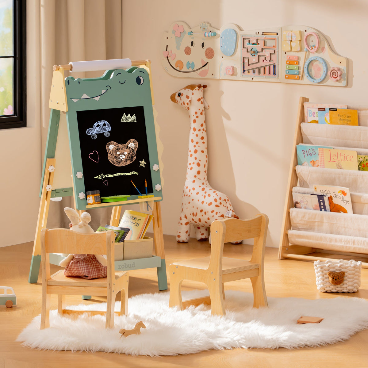 ROBUD dino easel and natural wood storage shelf in a pale playroom with a fluffy white rug and stuffed giraffe nearby.