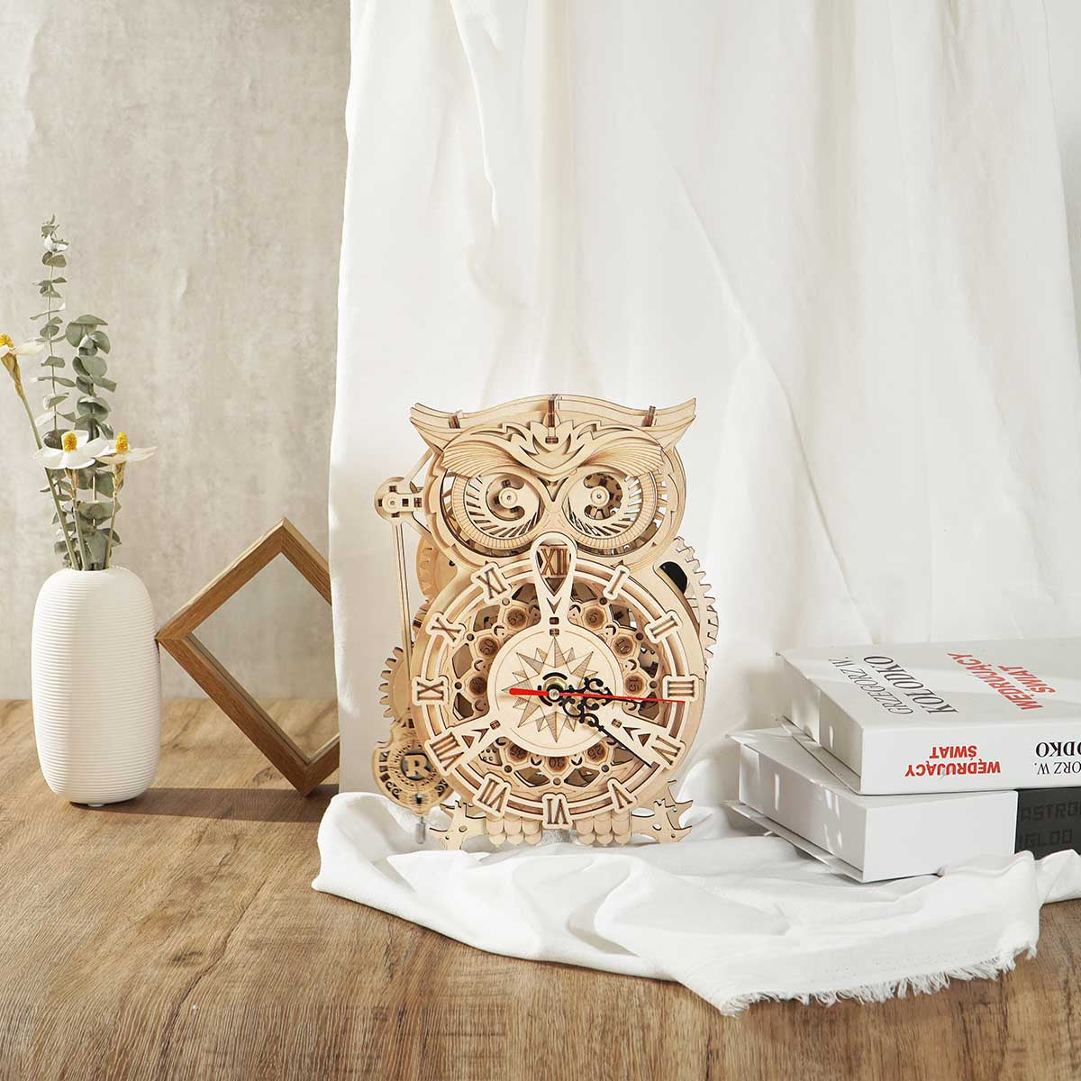 ROKR Owl Clock beside dried flowers in a white vase, placed against sheer white curtains in soft natural light