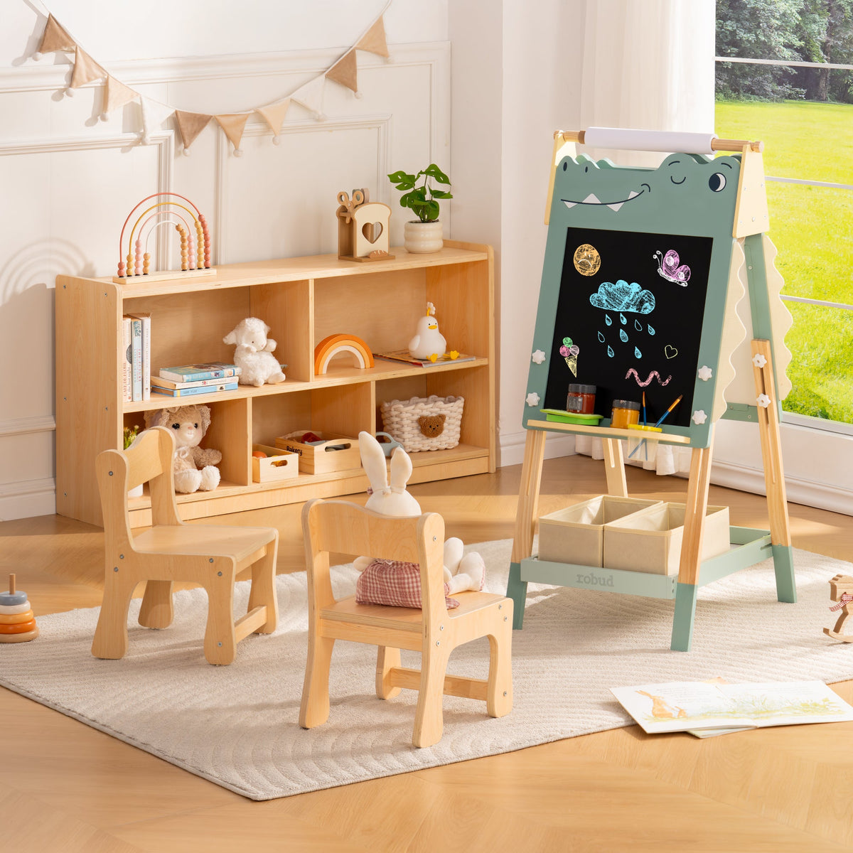 ROBUD natural wood table two chairs and bookshelf arranged in a playroom with a green dino art easel nearby.
